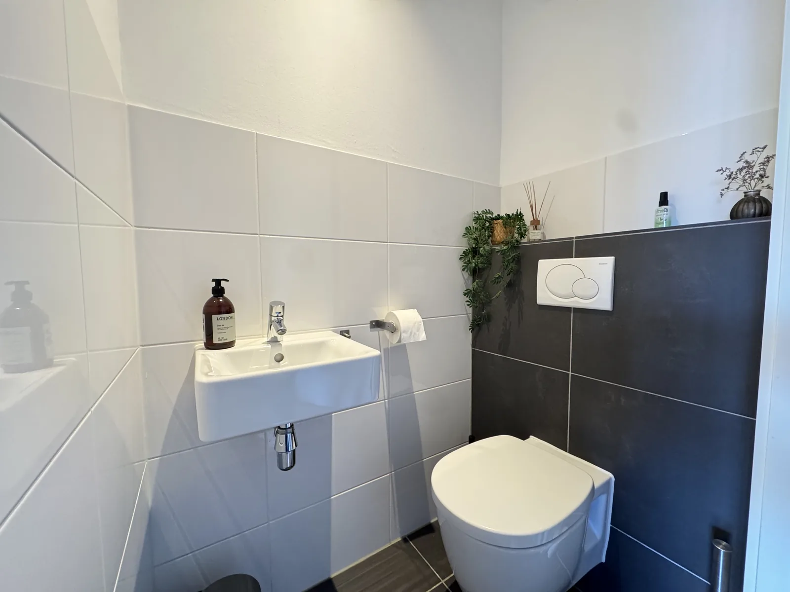 Separate guest toilet with wall-mounted WC, hand basin, and dark accent tiles in furnished Utrecht apartment