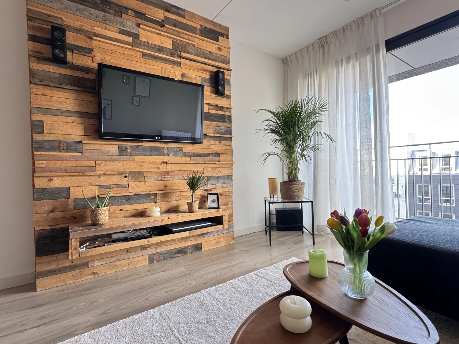 Reclaimed wood accent wall with mounted TV, decorative plants, and tulips on coffee table in furnished Utrecht apartment