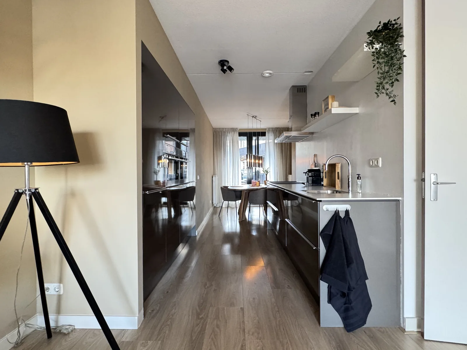 Modern galley kitchen with glossy dark cabinets, designer floor lamp, and dining area in Utrecht rental apartment