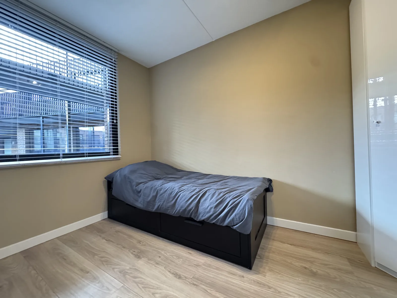 Second bedroom with single bed, venetian blinds, and city view window in furnished Utrecht expat apartment